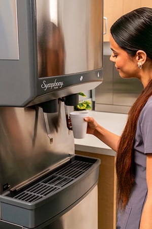 Nurse filling a cop of ice and water from a Follett Symphony Plus dispenser at a nurse's station